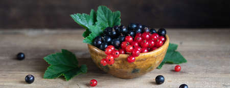 Red and black currant berries in ceramic bowl on a wooden background, toned vintageの写真素材