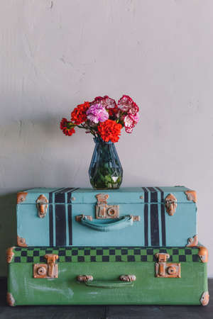 A pair of old vintage colored in blue and green suitcases, trunks, a vase with red flowers, travelling postcard conceptの写真素材