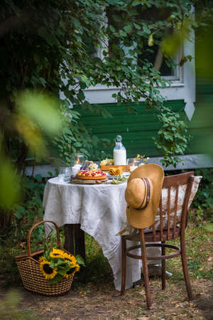 Traditional homemade plum cake or pie, summer table setting with milk, fruits, candlesの写真素材