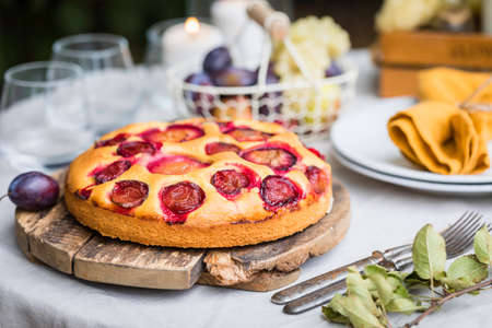 Traditional homemade plum cake or pie, summer table setting with fruits, candlesの写真素材