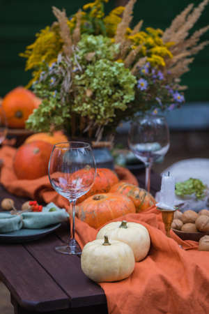 Fall themed holiday table setting arrangement for a seasonal party, glasses, pumpkins, candles, field flowersの写真素材