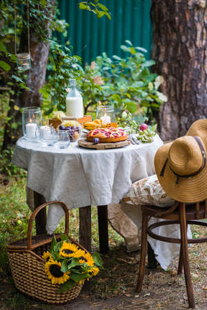 Traditional homemade plum cake or pie, summer table setting with milk, fruits, candlesの写真素材