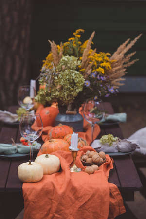 Fall themed holiday table setting arrangement for a seasonal party, glasses, pumpkins, candles, field flowersの写真素材