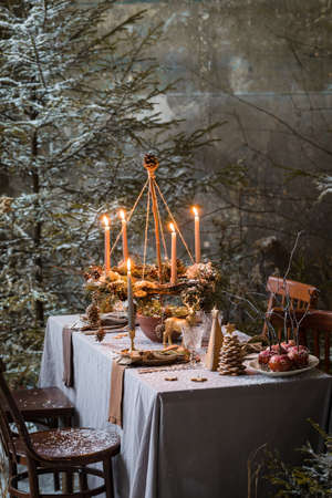 Table served for Christmas dinner, festive setting with decorations, burning candles and fir-tree branches, glassesの写真素材