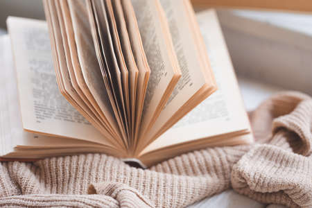 Warm and cozy hygge concept with white and beige sweater, old opened book on a windowsill, tonedの写真素材