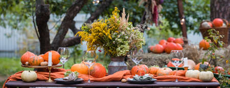 Fall themed holiday table setting arrangement for a seasonal party, glasses, pumpkins, candles, field flowersの写真素材