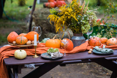 Fall themed holiday table setting arrangement for a seasonal party, glasses, pumpkins, candles, field flowersの写真素材