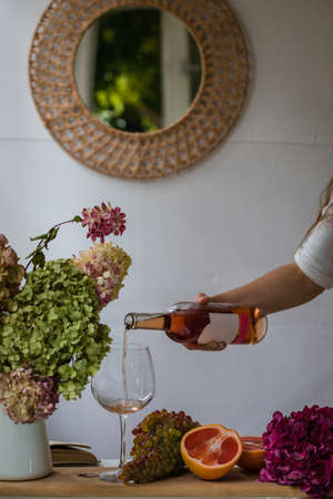 Woman's hand holding a bottle of wine and pouring in a glassの写真素材
