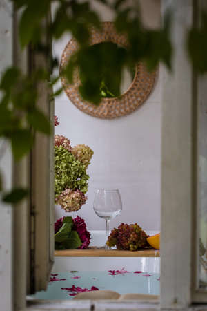 A view from the outside to the Bath tub with flower petals, grapefruit slices, bunch of grapes and a glass.の写真素材