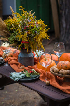 Fall themed holiday table setting arrangement for a seasonal party, glasses, pumpkins, candles, field flowersの写真素材