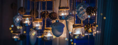 Warm and cozy Christmas window handmade natural style decoration with a garland made of glass jars, candles, cones, ballsの写真素材