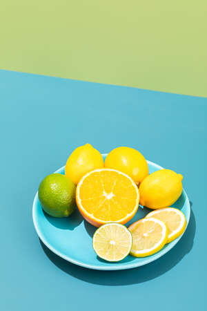 Minimalistic concept with slices of fresh lemons and limes isolated on a bright blue and green background, deep dark hard shadowsの写真素材