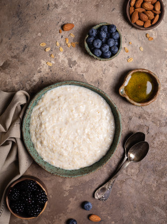 Oatmeal porridge with nuts, fresh berries and honey in a ceramic bowl on rustic backgroundの写真素材