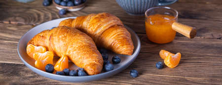 Breakfast with croissants, fresh blueberries, tangerines and jam on the wooden backgroundの写真素材