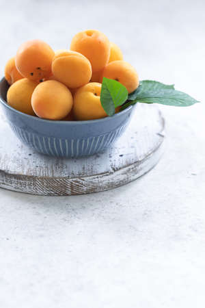 Fresh apricots in a blue bowl on a white wooden backgroundの写真素材