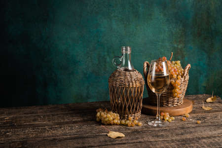 A glass of fresh homemade white wine with grapes and a bottle on a rustic wooden table, copyspaceの写真素材