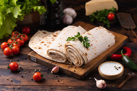 Lavash rolled on a wooden board, thin traditional oriental bread, Armenian flatbread, vegetables, cheese, greens and sauce, rustic backgroundの写真素材