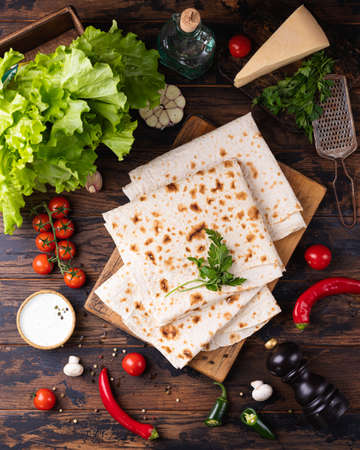 Lavash rolled on a wooden board, thin traditional oriental bread, Armenian flatbread, vegetables, cheese, greens and sauce, rustic backgroundの写真素材