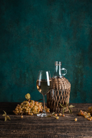 A glass of fresh homemade white wine with a bunch of grapes and a bottle on a rustic wooden table, copyspaceの写真素材