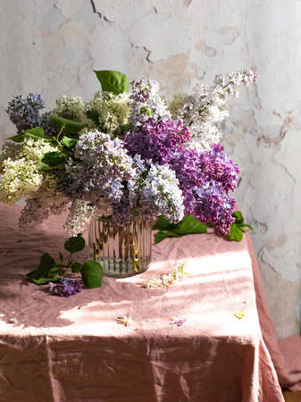 Vase with fresh multicolored lilac flowers on the linen fabric table-cloth with a sunshine daylight, spring and summer holidays postcard conceptの写真素材