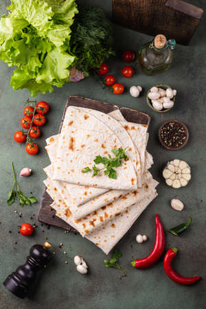 Lavash rolled on a wooden board, thin traditional oriental bread, Armenian flatbread, vegetables, cheese, greens and sauce, rustic backgroundの写真素材