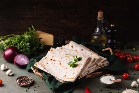 Lavash rolled on a wooden board, thin traditional oriental bread, Armenian flatbread, vegetables, cheese, greens and sauce, rustic backgroundの写真素材