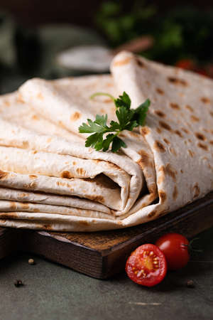 Lavash rolled on a wooden board, thin traditional oriental bread, Armenian flatbread, vegetables, cheese, greens and sauce, rustic backgroundの写真素材
