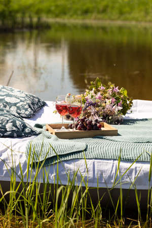 Romantic summer lunch picnic with flowers and glasses of wine on a mattress bed floating in the lake or pond, wellbeing and leisure conceptの写真素材