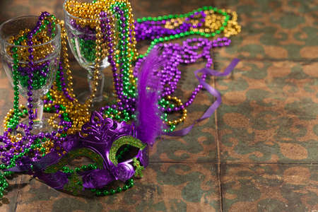 Colorful festive mardi gras or carnivale green, violet and yellow beads in glasses as decoration on a rustic tile background, selective focus, copyspace, postcardの写真素材