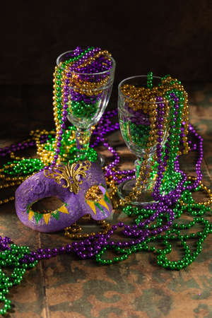 Colorful festive mardi gras or carnivale green, violet and yellow beads in glasses as decoration on a rustic tile background, selective focus, copyspace, postcardの写真素材