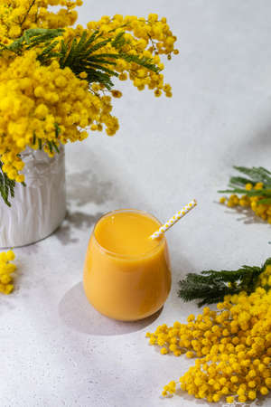 Orange Juice, citrus smoothie glass on spring background, with mimosa flowers vase, hard light, eco-friendly cocktail strawの写真素材