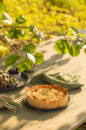 Golden organic healthy crispy pie quiche with artichokes, dried tomatoes and olives on the table, evening sunlight in the summer garden, soft selective focusの写真素材