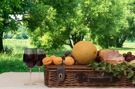 Wine, fruit, ham, basket on the background of trees and a pondの写真素材