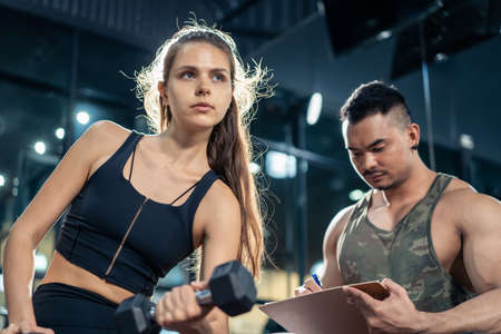 Asian Fitness trainer or instructor teach and motivate young Caucasian active sportswoman or athlete...