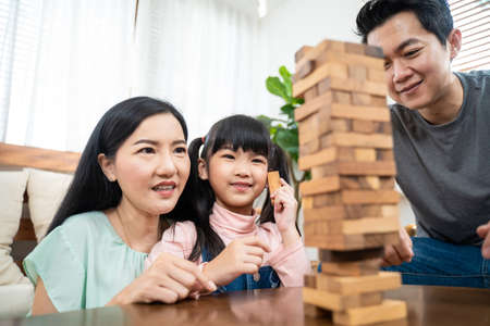 Portrait of Little small kid sitting in living room with family in house. Preschool girl daughter enjoy spend leisure free time with parents play toy block together. Love Relationship at home concept.の写真素材