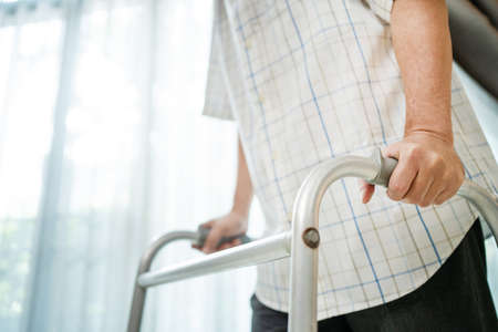 Close up hand of Asian Senior elderly disabled man patient walk slowly with walker at nursing home. Older handicapped male have weak leg use Zimmer frame to support. Medical therapy insurance concept.の写真素材