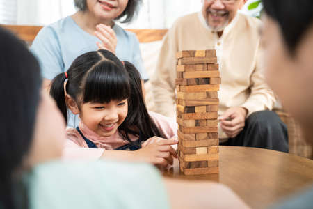 Asian happy family enjoy play toy block with little daughter in house. Grandparents and young loving couple parent having fun play Tumbling tower wood block game with cute kid girl in living room.の写真素材
