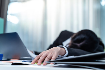 Exhausted Asian business woman office worker nap on desk at workplace. Busy Employee worker girl feel tired of many paper work, lying and sleep on computer table to get rest for health and freshness.の写真素材