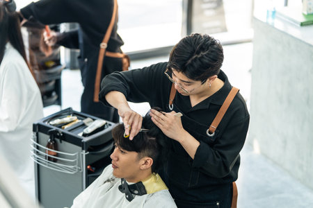 Asian hairdresser barber male cut hair of attractive man in salon shop. Professional hairstylist...