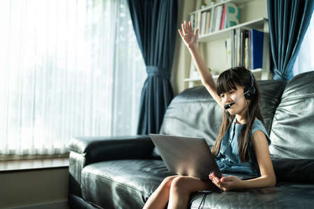 Homeschool Asian girl learn online class with virtual video conference. Little young kid look at laptop computer and study by digital remote meeting due covid19 pandemic from school teacher in house.の写真素材