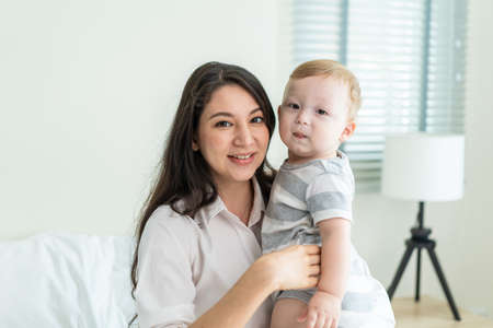 Portrait of Caucasian happy family smiling, look at camera in bedroom. Young attractive woman...