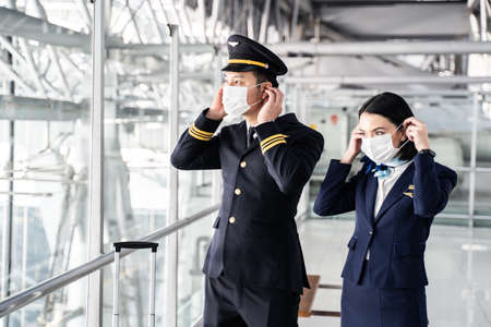Airliner pilot and air hostess wearing face mask walking in airport terminal to the airplane during the pandemic to prevent virus infection. New normal lifestyle in air transport conceptの写真素材