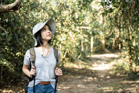 Asian young beautiful female backpacker traveling alone in forest wild. Attractive girl traveler look around and explore while walk in nature wood with happiness and fun during holiday vacation trip.の写真素材
