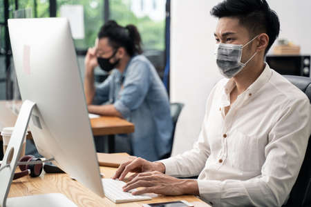 Group of Asian team business people working in office with new normal social distancing lifestyle concept. Man and woman wear protective face mask and keep distancing to prevent COVID virus in companyの写真素材
