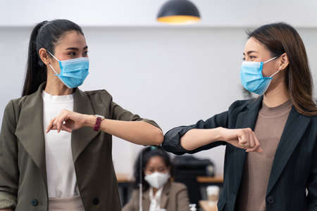 Two colleague female workers in office company have a greeting by touching the elbow or elbow bump...