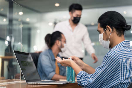 Group of Asian team business people working in office with new normal lifestyle concept. Man and woman wear protective face mask and keep distancing to prevent virus in company workplace.の写真素材