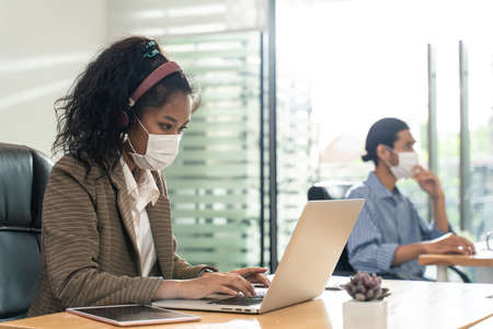 Group of Asian team business people working in office with new normal lifestyle concept. Man and woman wear protective face mask and keep distancing to prevent virus in company workplace.の写真素材
