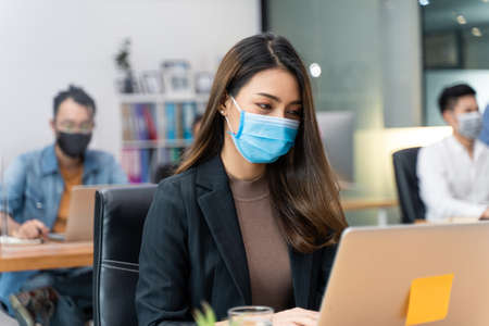 Group of Asian team business people working in office with new normal lifestyle concept. Man and woman wear protective face mask and keep distancing to prevent virus in company workplace.の写真素材