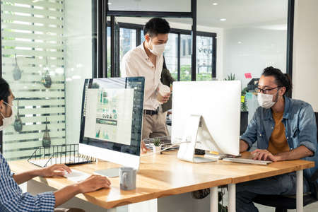 Group of Asian team business people working in office with new normal lifestyle concept. Man and woman wear protective face mask and keep distancing to prevent virus in company workplace.の写真素材