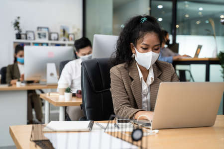 Group of Asian team business people working in office with new normal lifestyle concept. Man and woman wear protective face mask and keep distancing to prevent virus in company workplace.の写真素材